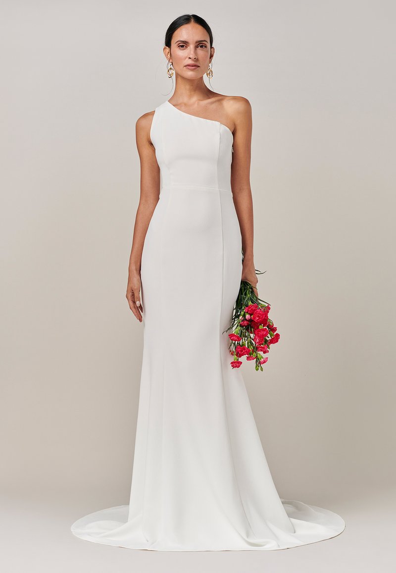 Vestido blanco de un solo hombro con una silueta ajustada, falda hasta el suelo y cola. La modelo sostiene un ramo de flores rosas. Textura suave.