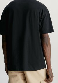 Černé bavlněné tričko s uvolněným střihem, krátkými rukávy a rovním lemem. Jednoduchý design, bez ozdob a vzorů.