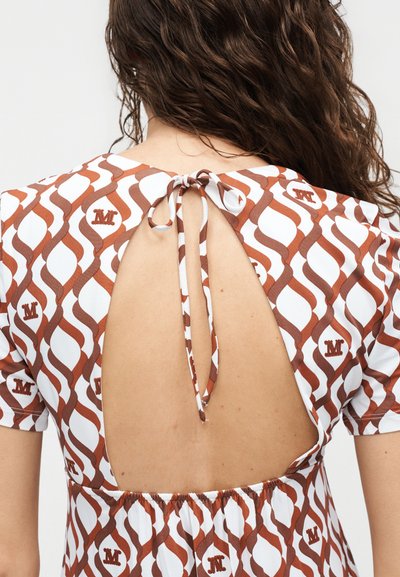 Καφέ και λευκό κοντομάνικο τοπ με ανοιχτή πλάτη δεμένη στον λαιμό, που φοριέται από ένα άτομο με μακριά καστανά σγουρά μαλλιά, στραμμένο προς τα πίσω.