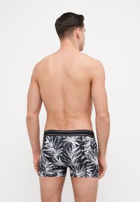 Boxer da uomo neri con un motivo di foglie tropicali bianche, vita elastica con un accento nero e un design aderente.