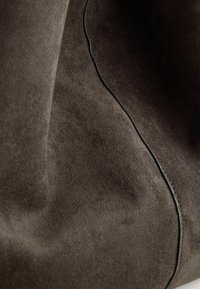 Material din suede maro cu o textură netedă, având un detaliu de cusătură neagră contrastant de-a lungul uneia dintre margini. Aspect moale și flexibil.