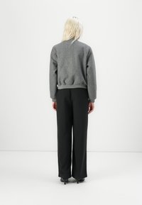 Maglione grigio a maglia con scollatura rotonda e polsini a coste, abbinato a pantaloni neri a gamba larga, mostrato da dietro su uno sfondo bianco.