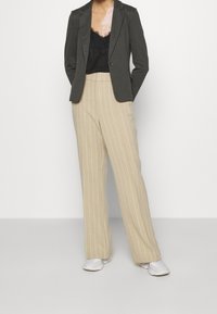 Szary, dopasowany żakiet noszony na czarnej koronkowej koszulce na ramiączkach, w zestawie z beżowymi, szerokimi spodniami w prążki i białymi trampkami.