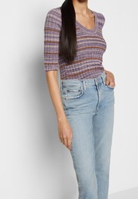 Lila randig stickad topp med korta ärmar och rundad halsringning, tillsammans med ljusblå högmidjade jeans. Slät textur och avslappnad passform.