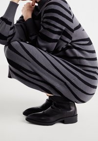 Grijze gebreide jurk met zwarte horizontale strepen, geribbelde manchetten en hoge halslijn. Zwarte enkellaarsjes met een gladde afwerking en blokhak.