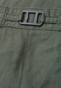 Tissu en lin vert foncé avec une boucle rectangulaire en plastique noir fixée à une sangle en tissu et des détails de couture cousus.