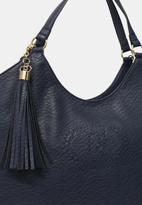 Borsa a tracolla in pelle blu navy con texture, hardware dorato, un nappino in pelle staccabile e un logo circolare in rilievo con borchie sul davanti.