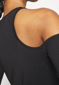 Schwarzes Sporttop mit kaltem Schulterdesign, glatter Stofftextur und rundem Ausschnitt mit kontrastierenden Nähten.