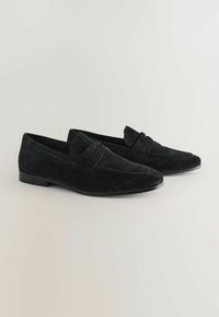 Schwarze Wildleder-Loafer mit glatter Textur, im praktischen Slip-On-Design und einem dekorativen Riemen über dem Vorderfuß. Flache Gummisohle für zusätzlichen Komfort.