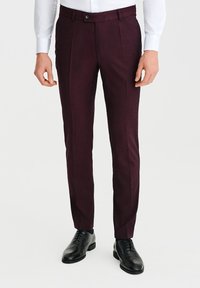 Bordowe spodnie o dopasowanym kroju, z gładką teksturą, dwoma frontowymi fałdami i jednym zapięciem na guzik, w komplecie z czarnymi butami wizytowymi.