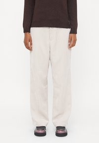 Pantalons en velours côtelé crème à jambes larges avec une surface texturée. Associés à un pull brun foncé et des chaussures noires imposantes.