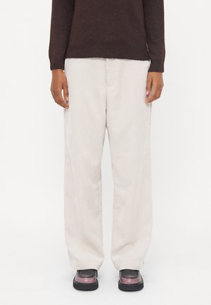 Pantalons en velours côtelé crème à jambes larges avec une surface texturée. Associés à un pull brun foncé et des chaussures noires imposantes.