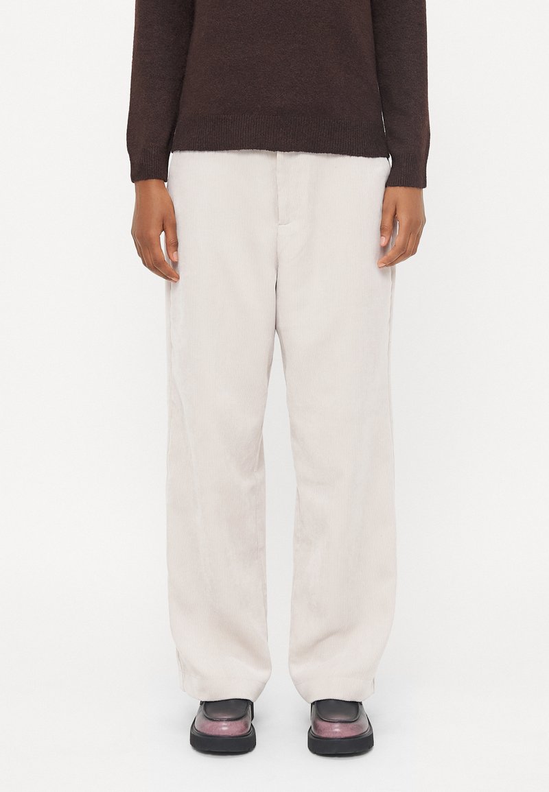 Pantalons en velours côtelé crème à jambes larges avec une surface texturée. Associés à un pull brun foncé et des chaussures noires imposantes.