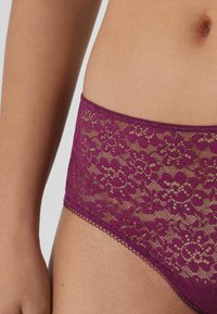 Krajkové bikinové kalhotky v tmavě fialové barvě, zdobené květinovými vzory a vlnkovým okrajem. Vyrobené z lehké krajky s hladkým povrchem.