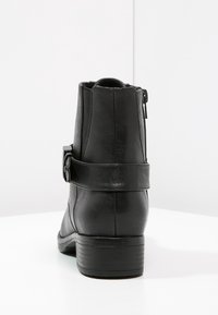 Stivaletto in pelle nera con finitura texturizzata, chiusura con zip laterale e dettaglio a cinturino attorno alla caviglia. Tacco a blocco e punta arrotondata.