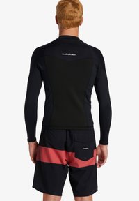 Čierny dlhý rukáv rash guard s textúrovaným chrbtom, spárovaný s čiernymi šortkami s horizontálnym červeným pruhom a zadnou kapsou.