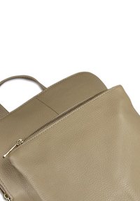 Beige leren backpack met een gestructureerde afwerking, voorzien van een ritsvak aan de voorkant en een verstelbare schouderband. Eenvoudig, modern ontwerp.