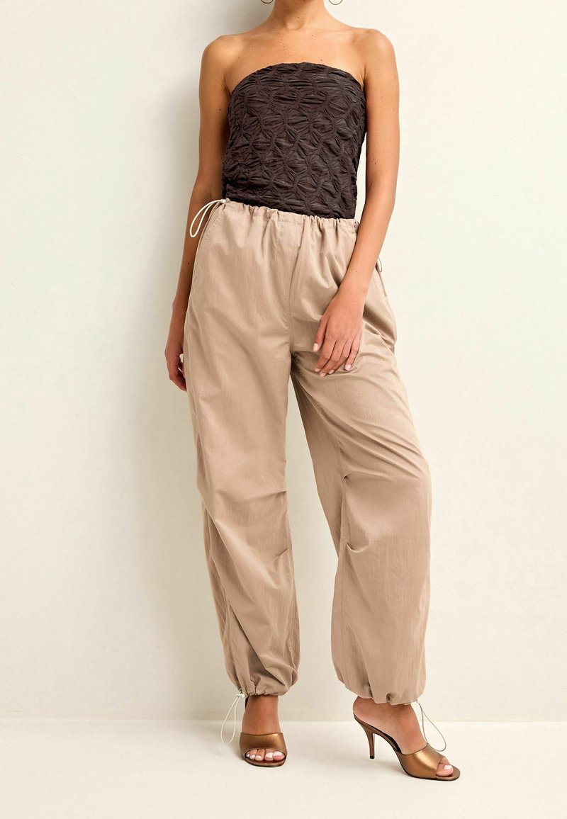 Strapless brun top med struktureret mønster, parret med beige bukser med elastisk talje og bronze høje sandaler med en samlet ankel detalje.