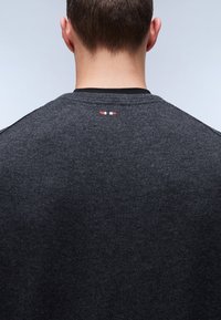 Pull gris foncé avec un tricot texturé et un col noir, avec un petit accent rouge, blanc et bleu à l'arrière du col.