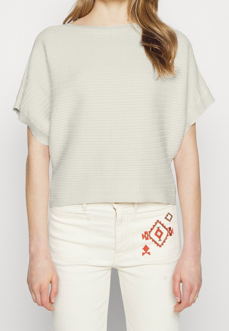 Light grey, short-sleeved sweater with ribbed texture, rounded neckline. Paired with cream-colored jeans featuring orange geometric embroidery.