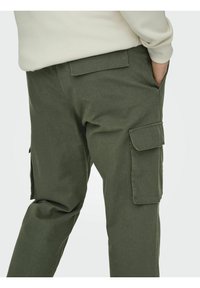 Olivgrüne Cargo-Hosen mit lässiger Passform, ausgestattet mit mehreren Seitentaschen, gesteppten Details und einer glatten Baumwollmischung.