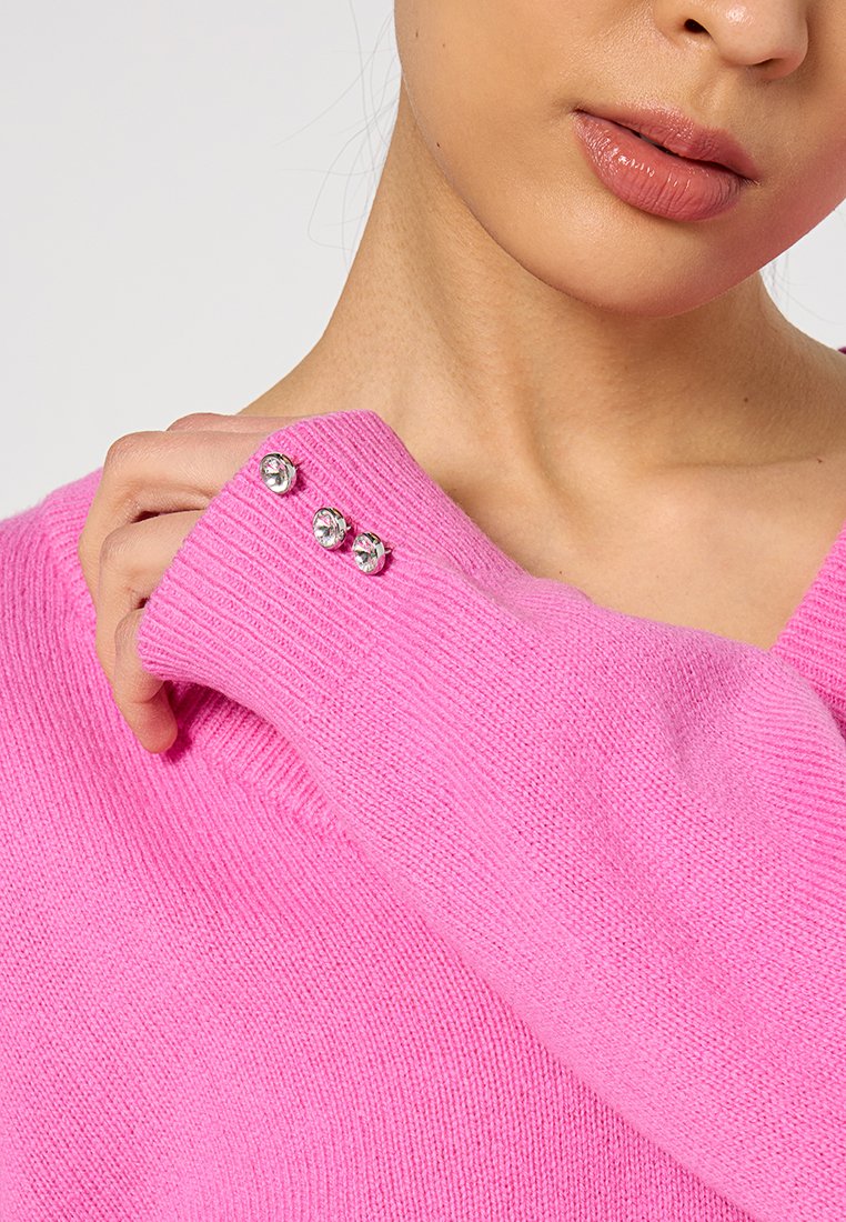 Suéter de punto rosa con mangas largas, textura acanalada y tres cristales decorativos en el puño. Diseño de escote en V.