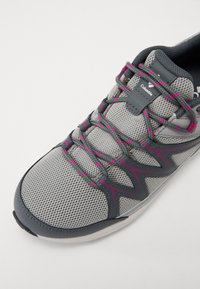 Gray athletic shoe with a mesh upper, fuchsia accents on laces and side design, and a sturdy rubber sole. Brand logo is visible on the tongue.