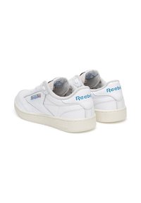 Adidași albi Reebok cu un superior din piele netedă, guler căptușit și talpă din cauciuc gri deschis. Prezintă accente ale logo-ului bleu pe călcâi și pe limbă.