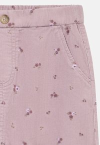 Tissu en velours côtelé rose avec un motif floral comportant de petites fleurs violettes et vertes. Comprend une poche avant et un détail de bouton à la taille.