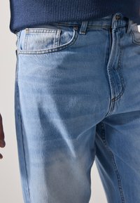 világoskék farmernadrág klasszikus fazonnal, épen megmaradt varrással és egy elülső zsebbel, enyhe fakulással és sima textúrával.