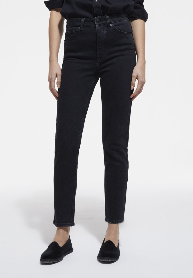 Jean noir taille haute avec une coupe ajustée, fabriqué en denim. Caractéristiques du design classique à cinq poches et ourlet brut à la cheville.