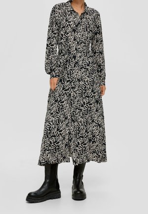 Czarna sukienka na guziki z długim rękawem w kremowy kwiatowy wzór, o luźnym fasonie i długości do połowy łydki, zestawiona z czarnymi masywnymi botkami.