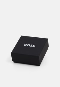Black square box with a matte finish, featuring silver embossed text "BOSS" on the top surface. Simple and elegant design.
