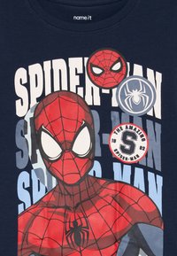 Spider-Man-Grafik mit roter Maske und Anzug, Spinnen-Logos sowie dem Text "SPIDER-MAN" und "The Amazing Spider-Man 1962" auf navyblauem Stoff.