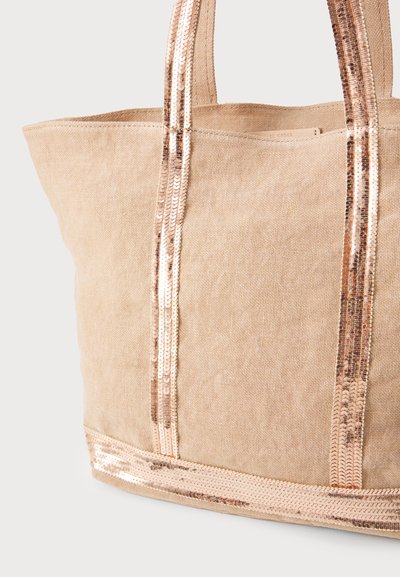 Sac fourre-tout en toile beige avec des anses en sequins rose doré brillants, présentant une large ouverture et un fond plat pour plus de stabilité.