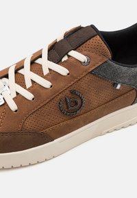 Brune lærersneakers med perforert design, lysebeige snører, mørkegrå tekstil detaljer, og et merke i svart.