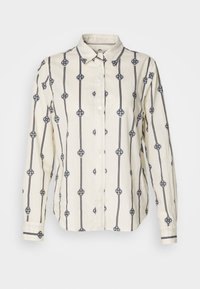 Langärmliges cremefarbenes Button-Up-Hemd mit schwarzen vertikalen Streifen und gleichmäßig verteilten kreisförmigen Knotenmuster auf dem Stoff.