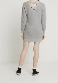 Grå stickad klänning med lång ärm, med en låg ryggdesign och korsande remmar samt ribbad kant vid fållen.