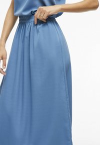 Jupe maxi bleu clair avec une taille élastique, présentant une texture lisse et douce ainsi que des plis sur les côtés pour plus de fluidité.