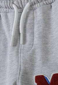 Grijze sweatpants met een trekkoord in de taille, geweven stof en een geborduurd "V" accent in het rood met blauwe details aan de zoom.