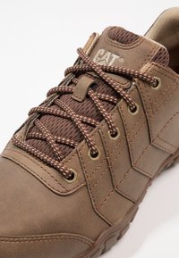 Braune Leder-Sneaker mit strukturiertem Mesh-Zungenteil, runden Schnürsenkeln, Metallösen und auffälligen Steppnähten. Gummisohle, die unter der Zehe hervorragt.