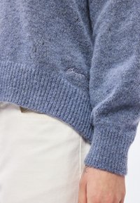 Ανοιχτό μπλε πλεκτό πουλόβερ με ριμπ τελείωμα και μανσέτες, κατασκευασμένο από μαλακό μείγμα μαλλιού. Διαθέτει μικρό κεντημένο λογότυπο κοντά στο τελείωμα.