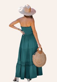 Teal strapless maxi-jurk met gelaagde ontwerpen, kantdetails en een smock-borstvoeding. Gepaarde met een ronde geweven tas en een strohoed met brede rand.