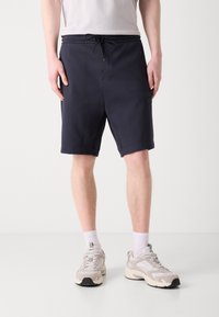 Marina blå bomullsshorts med elastisk midja och snörning, med sidofickor och en liten svart logotyp patch på vänster ben.