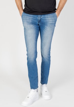 Vaqueros de mezclilla de un azul claro con corte ajustado, con una cintura de altura media, áreas desgastadas y un estilo clásico de cinco bolsillos. Combinados con zapatillas deportivas blancas.