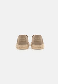 Beige Wildleder-Slipper mit einer gewebten Jutesohle und Markenlogo auf der Ferse. Glatte Textur und abgerundetes Design.