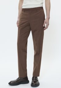 Barna nadrág texturált mintával, slim fit szabás, közepes derékmagasság, oldalsó zsebekkel, és sötétbarna mokaszinnal viselve.