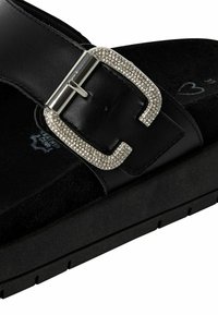 Sandalía de cuero negro con una correa texturizada, que presenta una gran hebilla metálica adornada con piedras de strass. Suela negra acolchada.