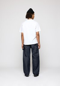 Hvid bomulds t-shirt med korte ærmer, parret med løstsiddende mørkeblå denim jeans med baglommer og kontrastsyning.