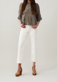 Haut en crochet gris à manches larges, associé à un pantalon blanc à jambes larges et des sandales compensées en cuir fauve avec une plateforme texturée.